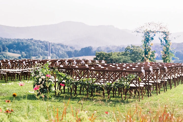 Pippin Hill Farm: A ceremony setup with wooden chairs, vines of greenery around them and pops up pink flowers at the beginning of the aisle.