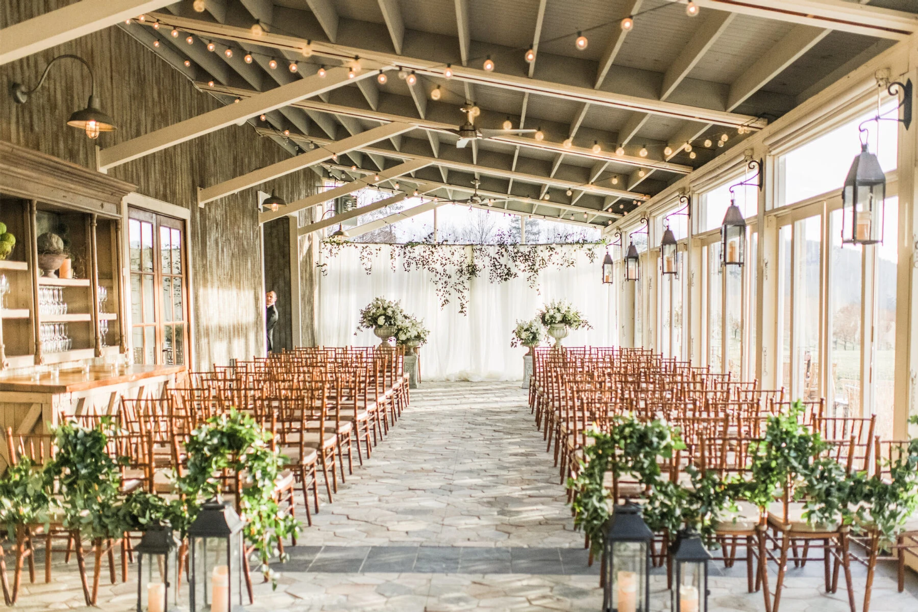 Pippin Hill Farm: An indoor terrace ceremony setup with wooden chairs and garlands of greenery hanging from the last row of chairs.