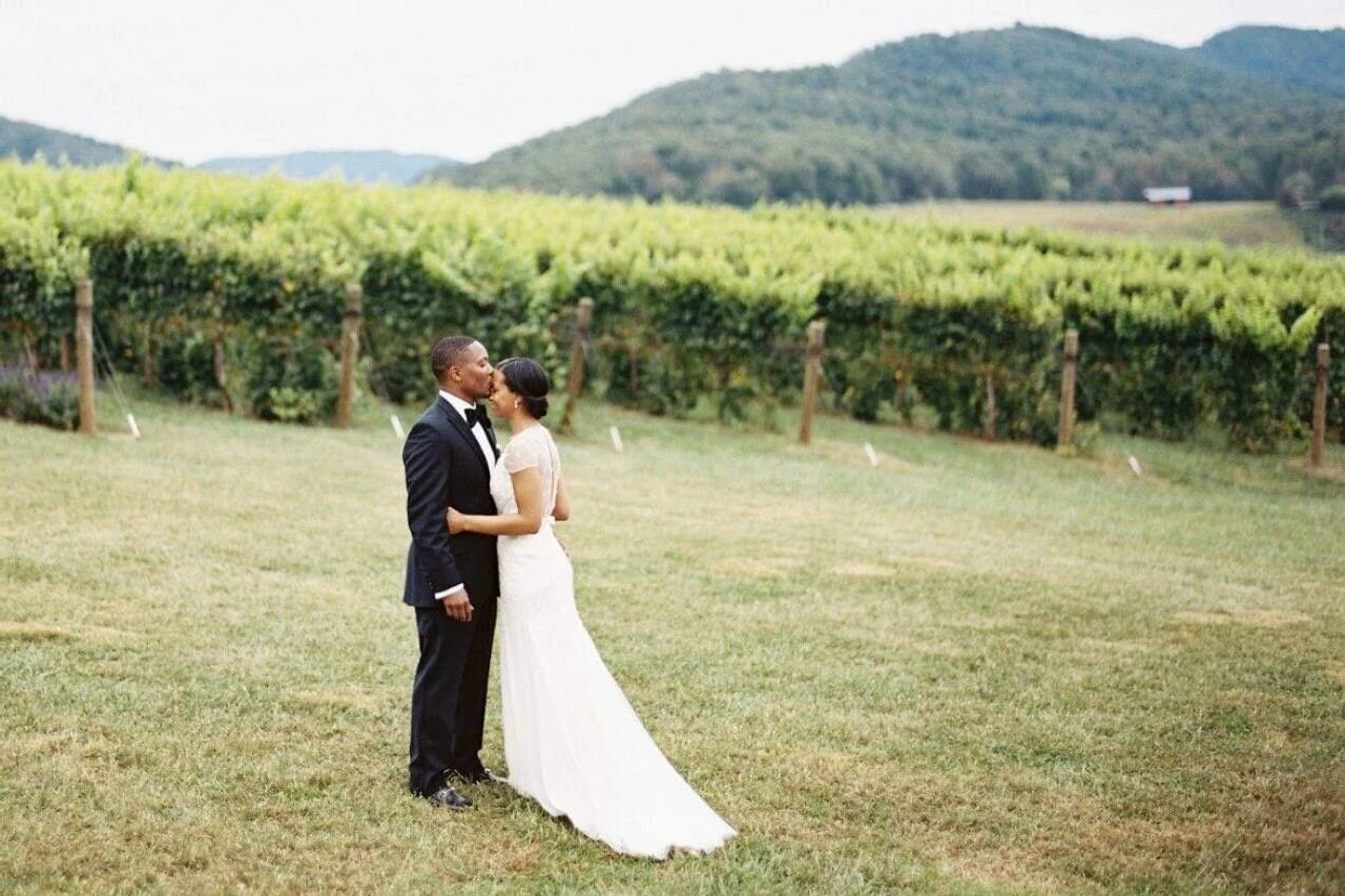 Pippin Hill Farm: A groom kissing a bride with a full view of vineyards and rolling hills in the background.