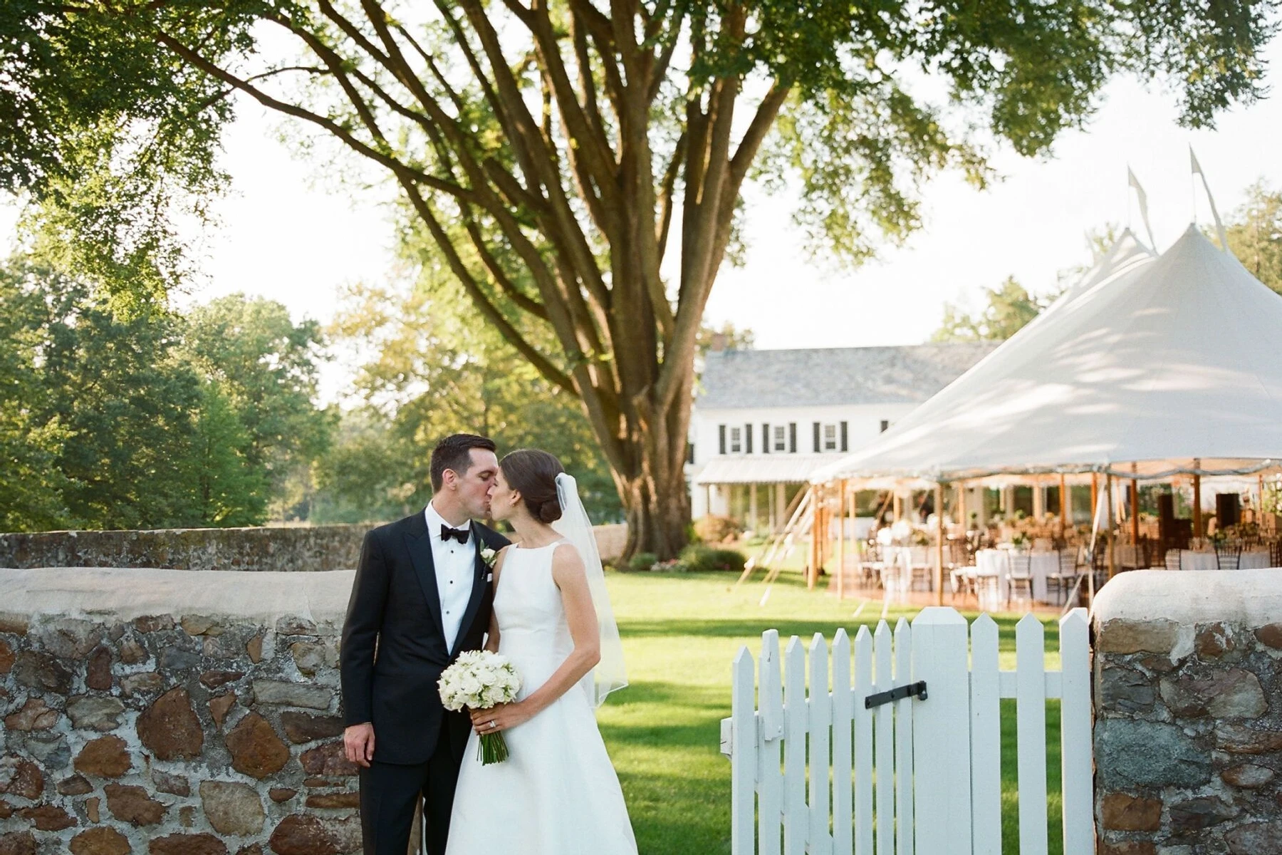 Tented Wedding Ideas: Couple in front of backyard tented wedding reception, featuring an open-air tent 