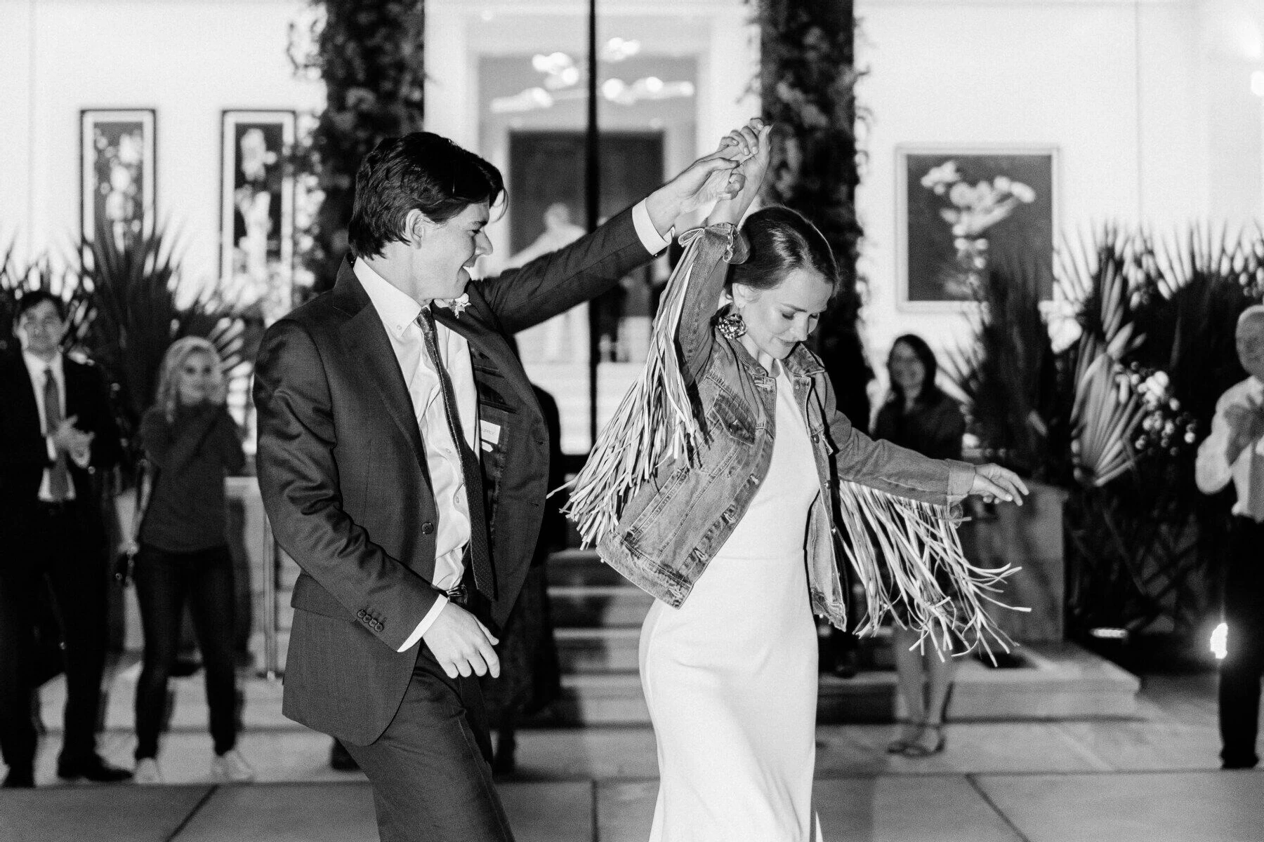 A groom spins his bride (wearing a fringed jean jacket) on the dancefloor during their rainbow wedding reception.