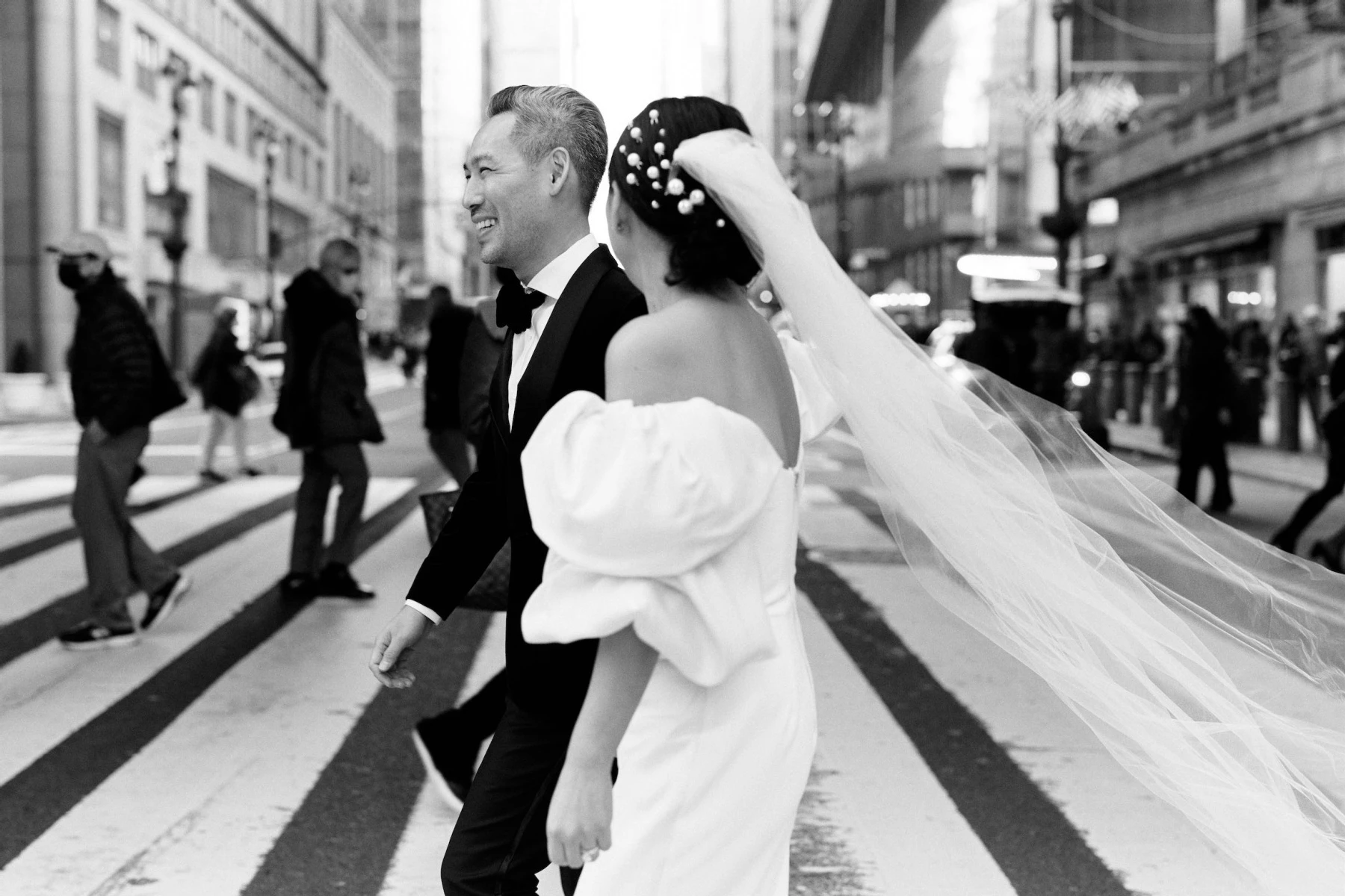 A black and white candid photograph of newlyweds crossing the streets of New York City on their way to their restaurant wedding reception.