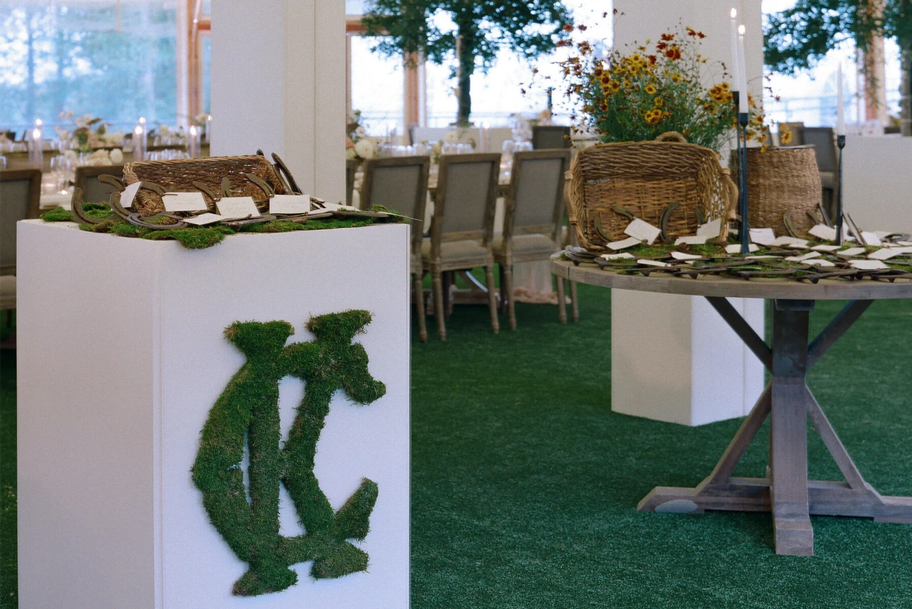 A monogram made of moss decorated a table holding escort cards at a rustic outdoor wedding.