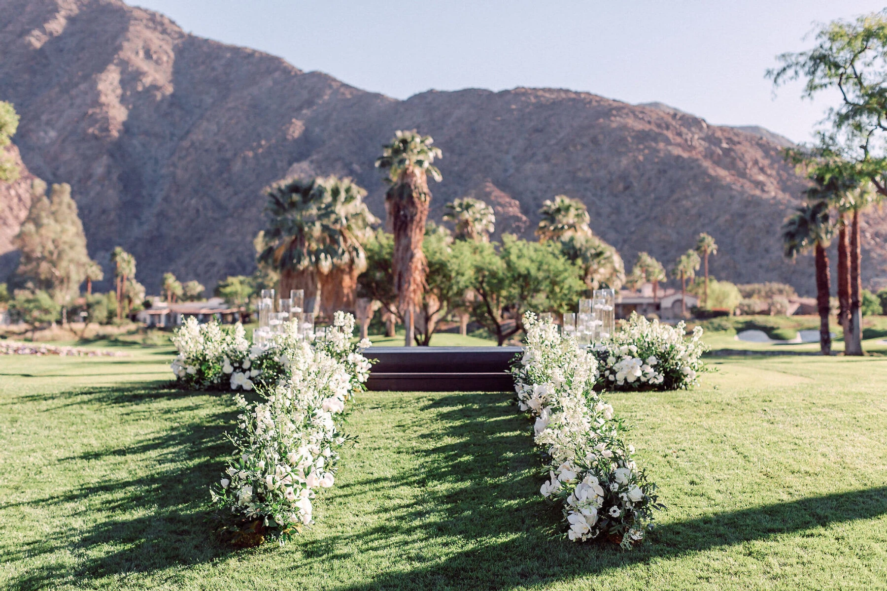 SEO for Wedding Venues: An outdoor ceremony aisle lined with white and green floral arrangements leading up to a podium, with palm trees and mountains in the background.