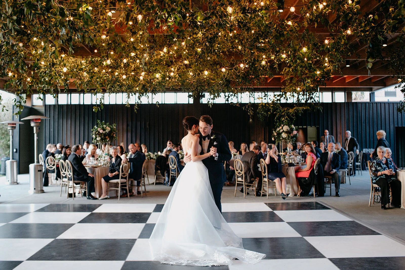 SEO for Wedding Venues: A wedding couple dancing on a white and black checkered dance floor with a greenery and light installation overhead.