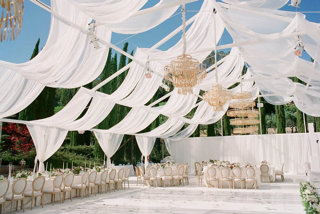 SEO for Wedding Venues: An open tented reception setup with a white dance floor, gold chandeliers, and billowing fabric hanging from the structure.