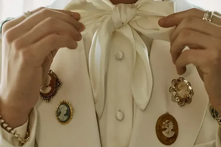 Close crop of an ivory suit with an ivory pussy-bow scarf tie and cameo brooches.