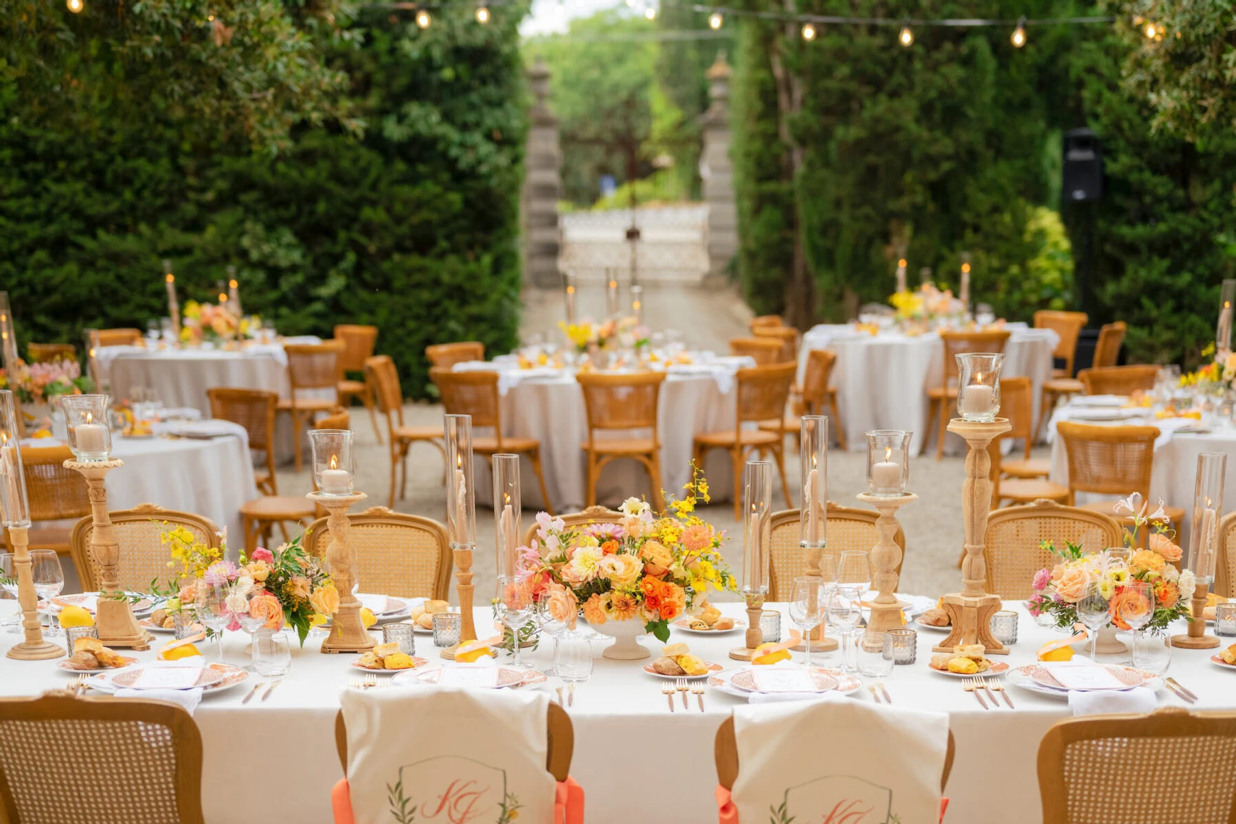 A Tuscan wedding reception decorated with centerpieces in shades of pink, orange, and yellow, with wooden candlestick holders.