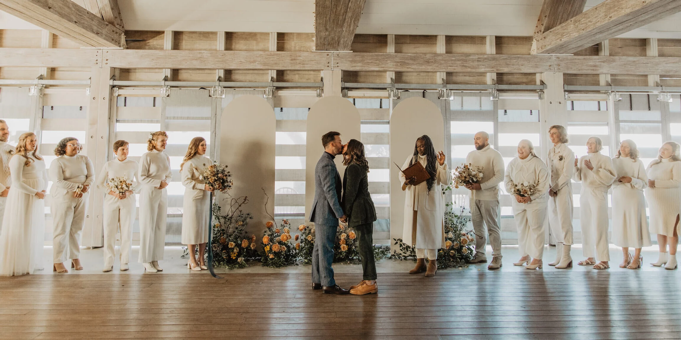 An untraditional wedding ceremony with the grooms in color flanked by their wedding party in shades of creamy white.