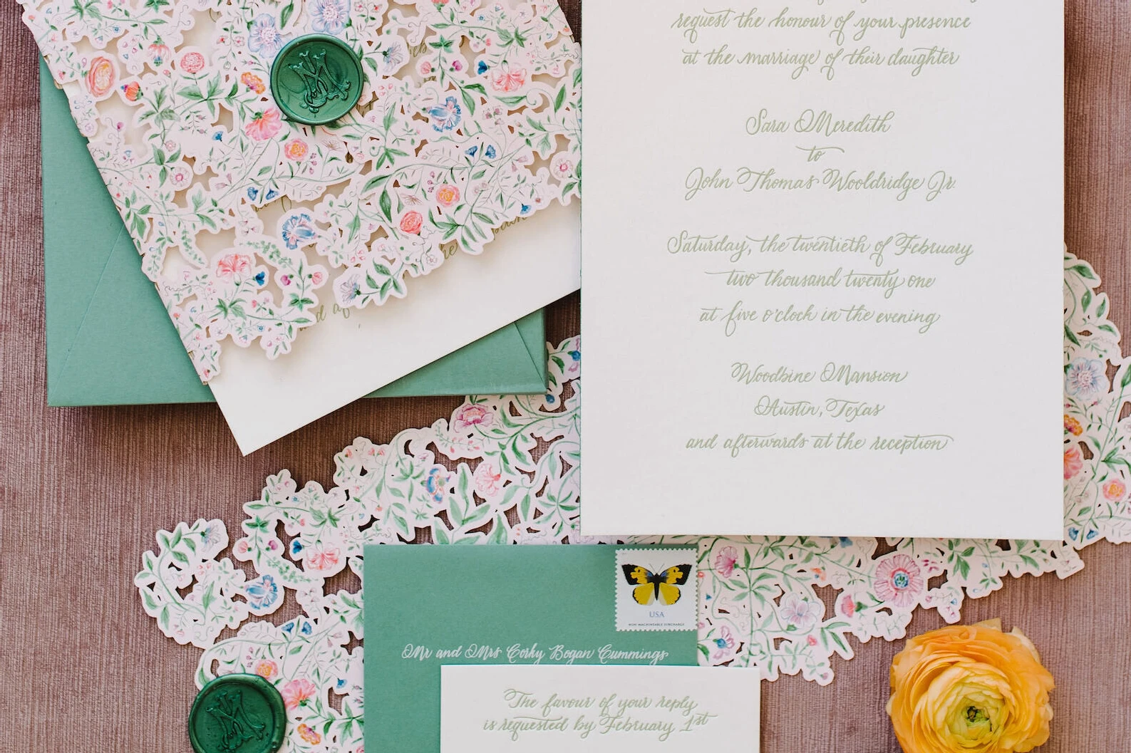 A wedding invitation suite with calligraphy and floral illustrations, and its soft green envelope ready to be sent using assorted vintage postage stamps.