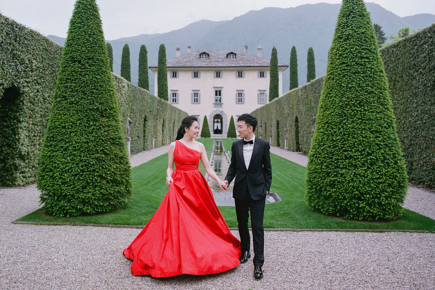 Wedding Dress Shopping: A bride in a red dress and groom holding hands and smiling at each other at an estate in Italy.