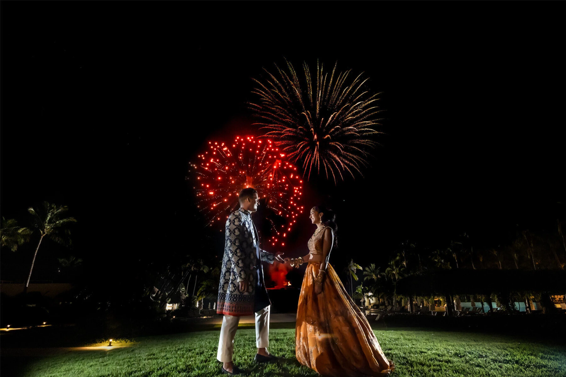 Wedding Fireworks Wedding Sparklers: A bride and groom smiling at each other while fireworks go off in the background.