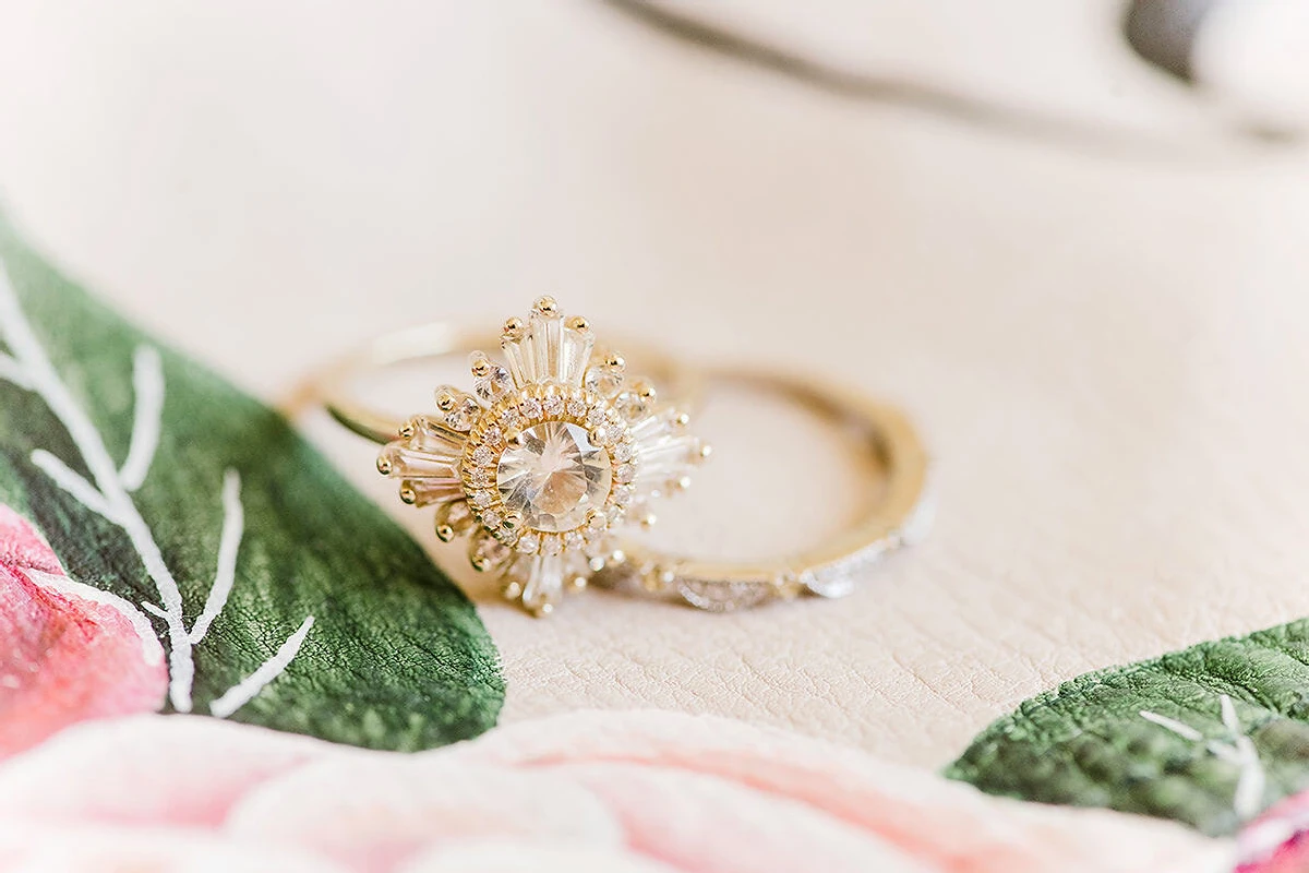 Wedding Ring Design: A beautiful star/flower inspired engagement ring next to a thin wedding band. Both rings are sitting on top of a flower design.