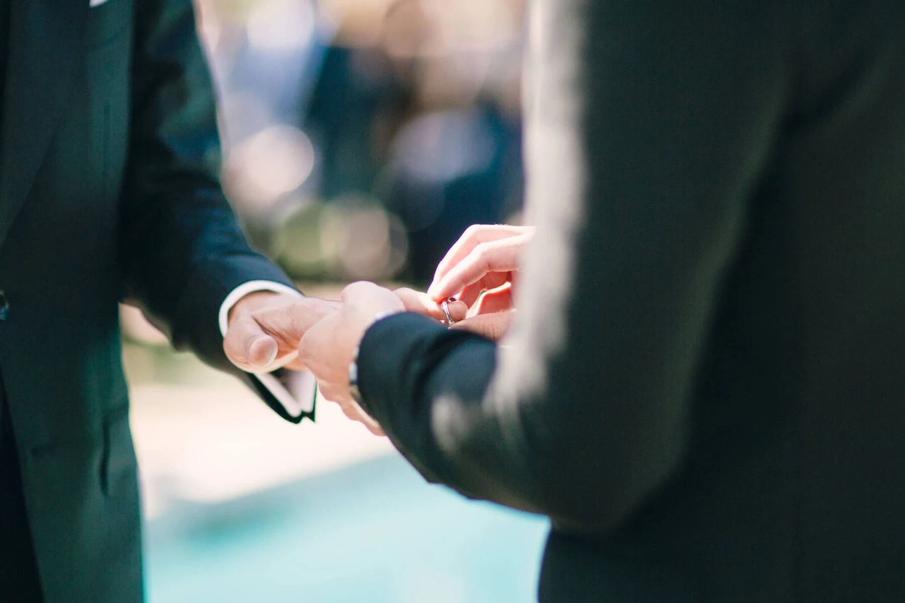 Wedding Ring Design: A groom placing a metal wedding band on another groom's finger.