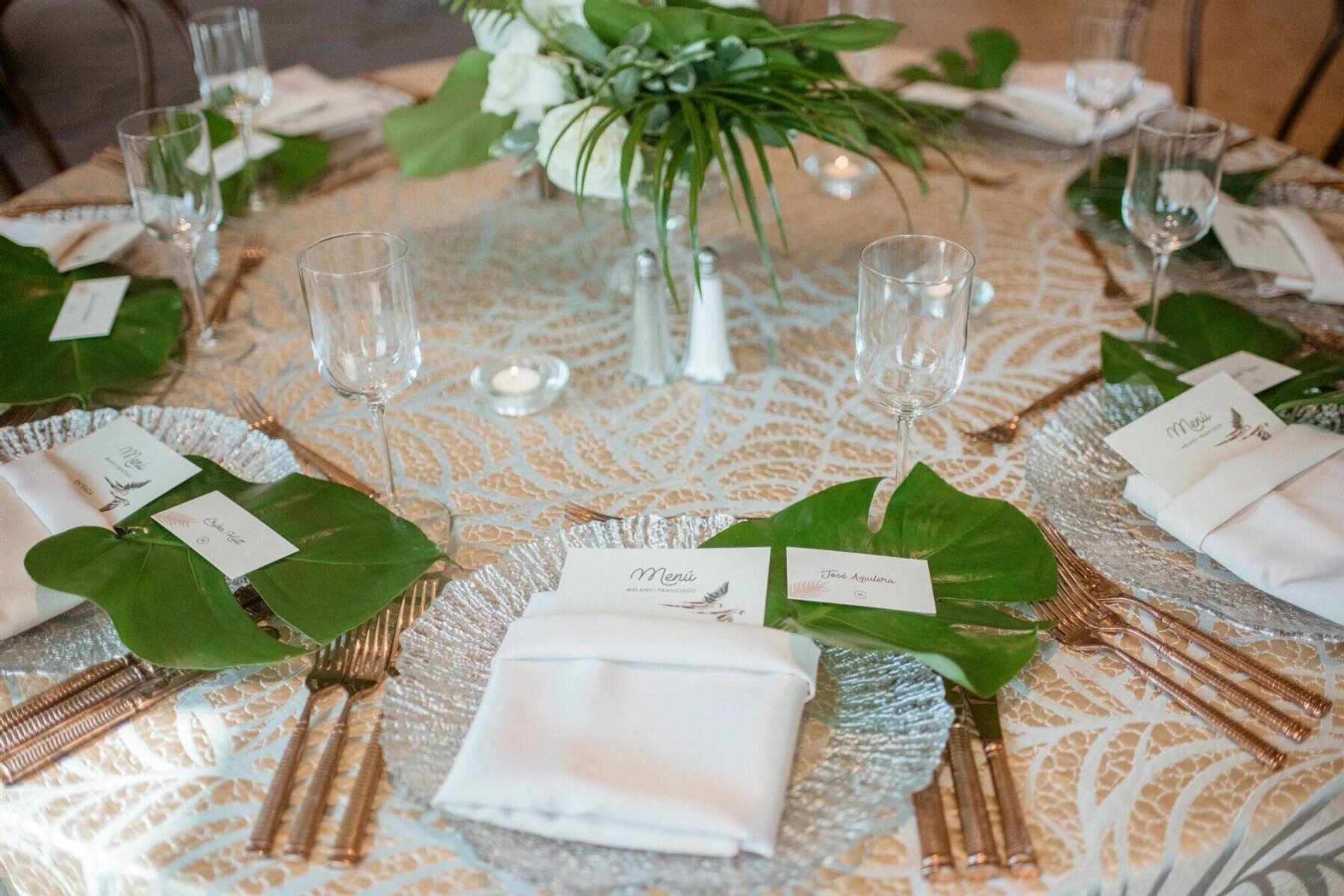 Wedding Website Examples: Another angle of wedding reception tables with oversize tropical leaves.