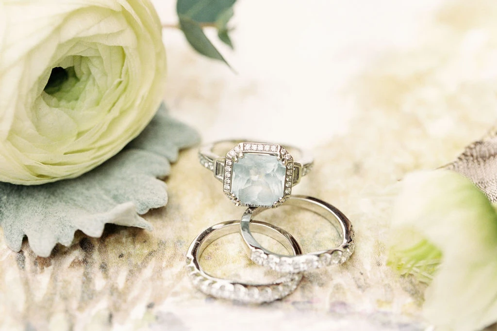 Wedding Website Examples: An up-close look at engagement and wedding rings with light green roses in the back.