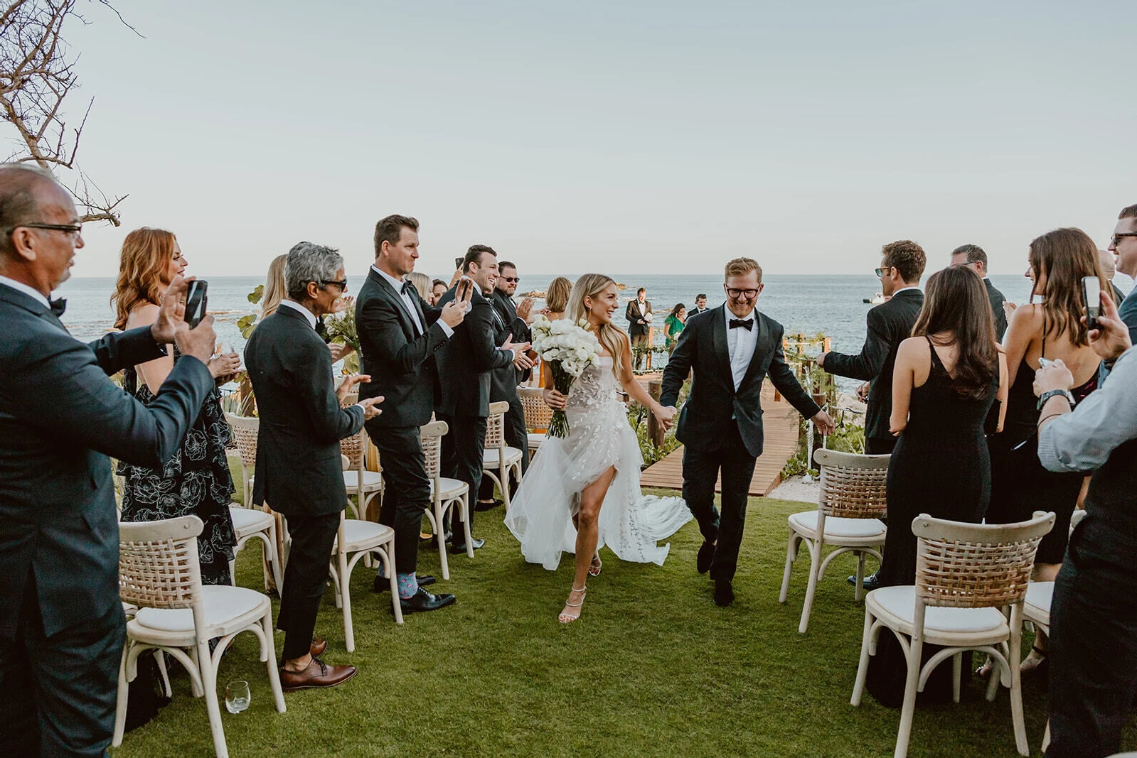 A pair of smiling newlyweds recess up the aisle after the ceremony of their Cabo wedding.